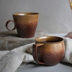 two brown cups sitting on top of a table next to a white cloth and vase