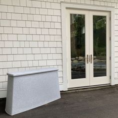 a white door sitting next to a window on the side of a building with a trash can in front of it