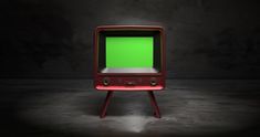 an old tv with a green screen sitting on top of a wooden stand in the dark