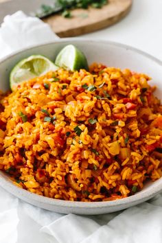 a white bowl filled with rice next to lime wedges and a wooden cutting board