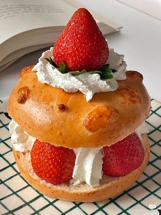 a pastry with strawberries and whipped cream on top is sitting on a table next to an open book