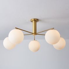 four white balls are hanging from a brass ceiling light fixture in a room with gray walls