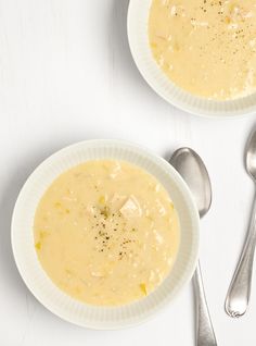 two white bowls filled with soup next to silver spoons on top of a table