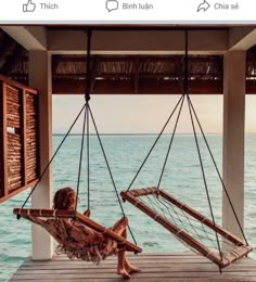 a little boy sitting in a hammock on a dock next to the ocean