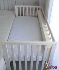 a small white crib in a bedroom next to a window with the sheets pulled down