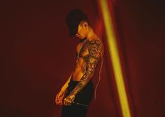 a man with tattoos on his arm and chest standing in front of a red background