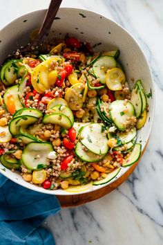 a white bowl filled with cucumbers, tomatoes and other veggies next to a blue napkin