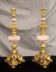 two pink and gold candlesticks sitting on top of a black table next to each other