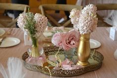 two vases filled with pink flowers sitting on top of a gold plated tray