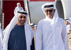 two men in white and blue outfits are walking towards the camera with other people behind them