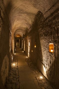 a long tunnel with lights on both sides and cobblestone walkway between two buildings