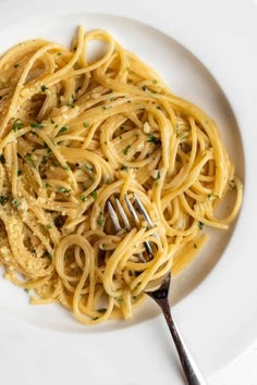 a white plate topped with pasta covered in sauce and parsley next to a fork