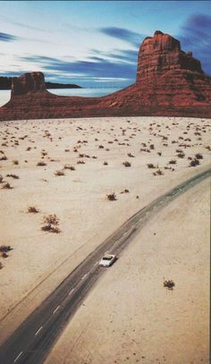 a car driving down a desert road in the middle of it's tracks and mountains