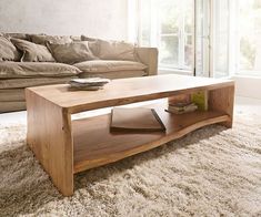 a wooden table sitting on top of a white rug in front of a couch and window