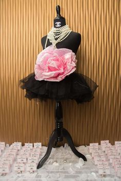 a mannequin with a pink flower and pearls on it's head sits in front of a wall