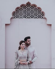 a man and woman standing next to each other in front of a wall with an arch