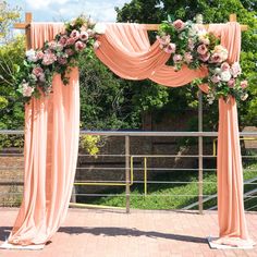 an outdoor wedding ceremony with pink drapes and flowers on the top, along with greenery