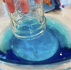 a person is pouring blue liquid into a glass bowl on a counter top with other items in the background