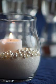 a glass vase filled with pearls and a lit candle