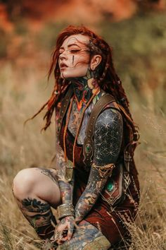 a woman with red hair and tattoos sitting in tall grass