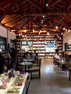 people sitting at tables in a library with lots of bookshelves and lamps hanging from the ceiling