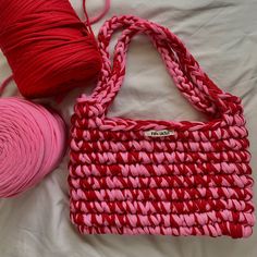 two balls of yarn sitting on top of a bed next to a pink bag and red ball of yarn