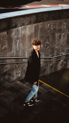 a young man walking down the street wearing jeans and a coat