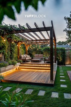 a wooden deck with lights under it in the middle of some grass and plants on either side