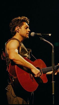 a man holding a guitar while standing in front of a microphone and singing into a microphone