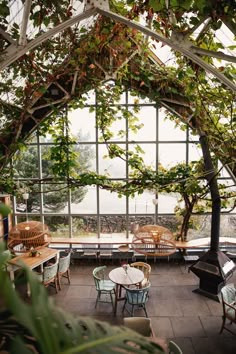 the inside of a restaurant with tables and chairs covered in ivys, surrounded by large windows