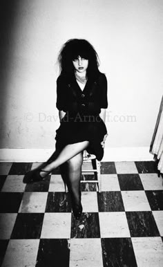 black and white photograph of a woman sitting on a checkered floor with her legs crossed