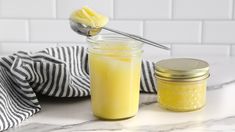 a glass jar filled with yellow liquid next to a spoon on a marble counter top