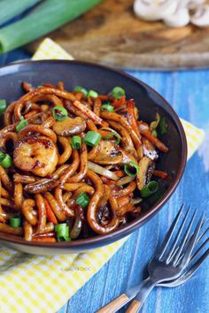 a bowl filled with noodles and vegetables on top of a table next to silverware