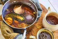 a pot filled with soup next to two mugs on a wooden table and cloth