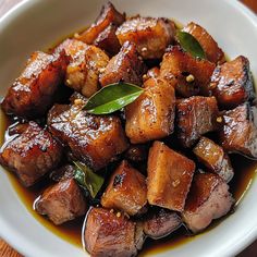 a white bowl filled with cooked meat and sauce on top of a wooden table next to a fork