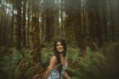 a woman sitting in the middle of a forest surrounded by tall trees and ferns