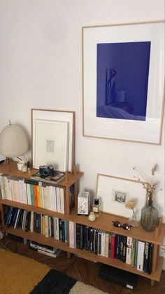 a bookshelf filled with lots of books next to a lamp and pictures on the wall