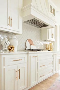 a kitchen with white cabinets and gold trim on the counter tops, along with an oven hood