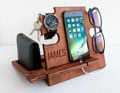 an iphone, watch, and glasses are on a wooden stand with a cell phone in it