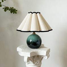 a green lamp sitting on top of a white table next to a vase and plant