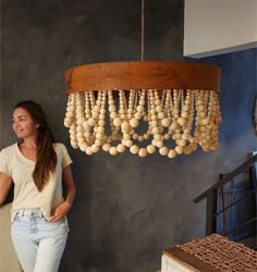 a woman standing next to a chandelier made out of wooden balls and beads