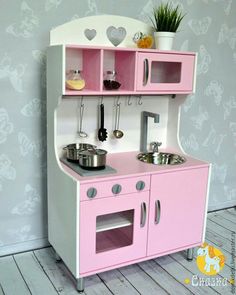 a pink and white play kitchen with pots and pans on the stove top oven