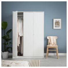 a white wardrobe with clothes hanging on it and a chair next to it in front of a blue wall