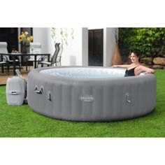 an inflatable hot tub sitting on top of a lush green field next to a woman