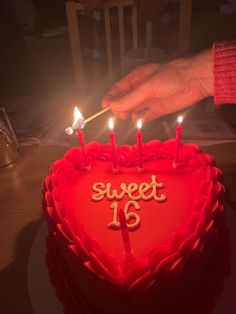 someone lighting candles on a heart shaped cake with the word sweet sixteen written on it