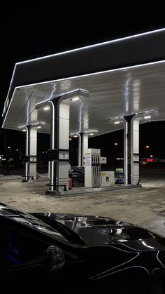 an empty gas station at night with cars parked in the parking lot and lights on