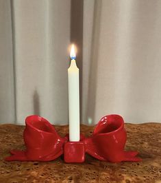 a white candle with a red bow around it sitting on a table next to a curtain