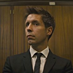 a man wearing a suit and tie in front of a wooden wall with wood paneling