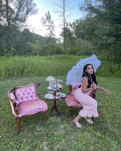 a woman sitting in a chair with an umbrella next to a pink couch and table