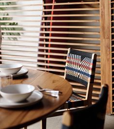 a wooden table topped with white plates and bowls next to a window covered in blinds